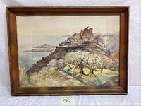 Framed watercolor painting showing a village on a mountain top with olive trees and sea in background.