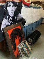Jim Morrison fabric wall hanging draped over a chair near a framed Jim Morrison orange and black wall art, and a metal rack holding black vinyl records.