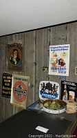 Wide view showing multiple vintage beer signs on wood-paneled wall, beer trays on table, coasters, bar mat, and tap.