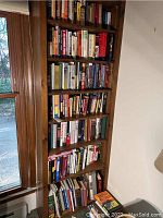 Bookshelf with multiple shelves filled with hardcover and paperback books of varying sizes and colors focused on history and WWII.