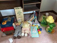 Wide shot showing all items in lot including dolls, box, birth certificate, books, board games, frog lamp, and dog face light switch plate cover