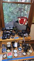 Overview photo showing all cameras, lenses, flash units, filters, and cases displayed on a wooden table in front of a window.