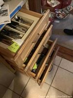 Three partially open wooden drawers showing cutlery organizers and flatware inside.
