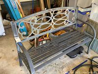 Full side and front view of the metal garden bench with decorative backrest and slatted seat and armrests.