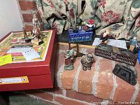 Overview of all items showing figurines, mechanical banks, model soldiers, and German soldier box on brick hearth.