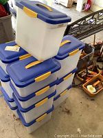 Stack of plastic storage bins with blue lids and yellow handles, showing dirt and wear.