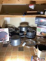 Overview of Calphalon pots, pans, and lids spread out on floor with packaging and Circulon stove top grill box showing.