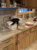 Overview of countertop with various baking and mixing dishes including Pyrex and Corning Ware items, some stacked and some with lids visible.
