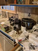 Photo showing various small kitchen appliances including blenders, coffee grinder, hand mixer, crockpot and slow cooker placed on kitchen counter.