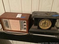 General Electric radio and 8-day mantel clock displayed side by side on a surface, wood case of radio shows marks and scratches, clock with key on top.