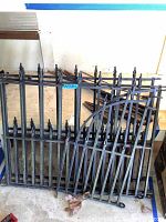 Five wrought iron style fencing sections stacked upright against a wall indoors. Sections are black metal with decorative pointed finials on vertical bars. Some sections have curved tops with scrollwork.