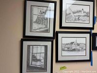 Four framed and matted seashore prints hung on a beige wall showing coastal and lighthouse scenes in black and white.