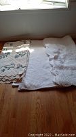 Three bedspreads laid flat on wooden floor: one floral and two white quilted bedspreads.