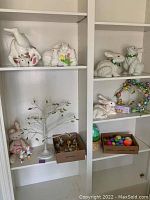 Shelf displaying ceramic bunny figurines, Easter tree decorated with pastel lights and plastic eggs, and stuffed bunny toy
