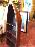 Front view of canoe-shaped shelf with three removable shelves inside, copper-colored exterior with riveted trim.