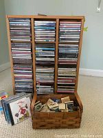 Wooden rack with over 100 CDs in jewel cases, arranged vertically in three columns. Large woven basket full of souvenir matchbooks in front of rack.