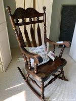 Side view of solid wood rocking chair showing dark finish, curved armrests, and two decorative pillows on seat.