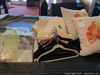 Show stacked sheets, blankets, floral throw pillows, curtains, clothes hangers on table or couch.