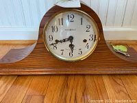 Front view of the wooden mantel clock showing the dial with Arabic numerals, clock hands and 'Howard Miller' branding.
