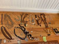 Wide shot showing various necklaces, earrings, bracelets, and pendants arranged on a wooden floor against white beadboard.
