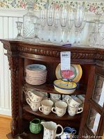 Wooden antique cabinet with Johnson Brothers china cups and saucers, and decorative plates inside.