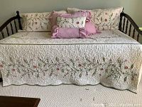 Front view of day bed showing quilted floral cover and arrangement of pillows and shams.