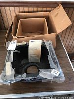 Original cardboard box with black Kohler bar sink inside, wrapped in plastic packaging, instruction manual visible inside the sink.