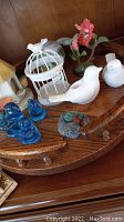 First wooden lazy susan showing white ceramic birds, birdcage, blue glass birds, and bird's nest decoration.