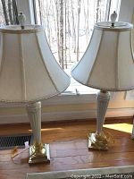 Pair of lamps positioned on hardwood floor in front of a window showing full height and matching design.