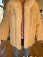 Front view of white mink coat worn by person, showing the coat extends to upper thigh with a plush creamy white fur texture and collar.