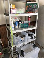 Full view of shelving with various household and garage items organized on shelves including spray paint cans, insect repellents, containers with cords, lightbulb box, and trash bag box.