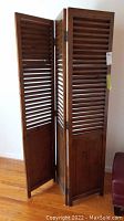 Three-panel foldable wooden screen angled showing louvered slats and solid bottom panel