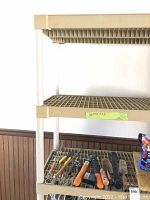 Front view of two tiers of beige plastic shelf with various hand tools on the bottom shelf, label with measurements attached on middle shelf.