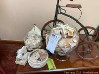Table with two glass containers full of seashells, metal and wood tricycle model visible behind, lighthouse coasters stacked in front.