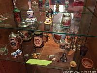 Display of glass cabinet containing assorted beer steins, shot glasses, souvenir items and miniature figurines.