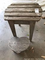 Top view of wooden slatted table showing weathered surface and sturdy legs, with small heart-shaped seat stool underneath.