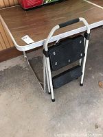 Folding table and folding step stool set shown, focusing on step stool leaning against table edge.
