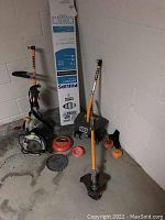 Full view showing Ryobi string trimmer, saw blades, trimmer line coils, and Philips fluorescent bulbs box in a basement corner.