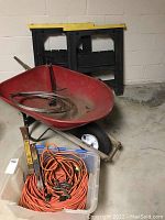 Photo of wheelbarrow, extension cords in plastic bin, and sawhorses against a basement wall