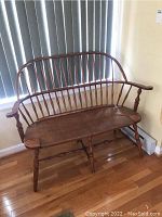 Front view of the wooden Windsor style bench showing turned legs, spindle backrest, and woven seat.