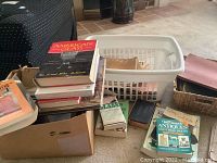 Stack of vintage and collector books on carpet and inside box, including one titled American Glass, stack includes newspapers and some loose papers as well.