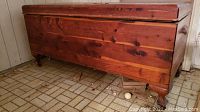 Side view of the West Branch cedar chest showing its rectangular shape, stained wood finish, and short decorative legs. Shows scuffs and scratches on the surface.