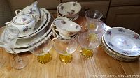 Photo showing stacked plates, bowls, tea cups, saucers, martini glasses, and etched yellow footed dessert cups on a wooden surface.