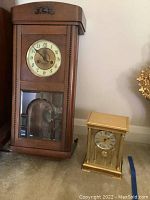 Vintage wood case wall clock and brass quartz mantle clock side by side
