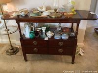 Front view of vintage Drexel wooden server with two drawers, shelf below, various decorative household items on top and shelf, some scratches visible on surface.