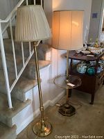Photo showing the full view of both the brass floor lamp with cream fabric pleated shade and the vintage glass and brass lamp table with cream fabric shade in an indoor residential setting.