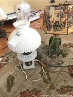 Wide view showing all five lamps together on carpeted floor. Includes milk glass lamp with hobnail base, oil lamps, green glass lamp, and lamp with painted shade.