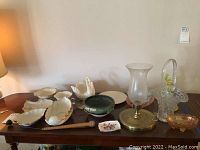 Wide view of the assembled items on a table including glass basket, glass lamp, Amber carnival glass, blue-green planter, porcelain leaf dishes, and candlesticks.