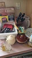 Photo of box with assorted kitchen utensils including oyster shuckers, knives in wood block, graters in packaging, and knives