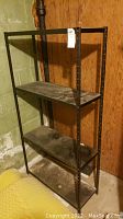 Full view of 4 tier metal shelving rack positioned in a basement corner against concrete and wooden walls. Shows dust and dirt accumulation on shelves.